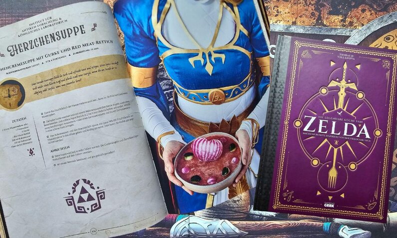 Detailansicht eines „Zelda“-Rezeptbuchs und einer Figur in einem königsblauen Outfit, die eine dekorative Suppe mit Zwiebelherz hält. | © Sabrina Forst