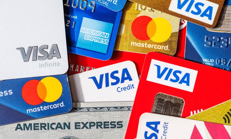 Verschiedene Kreditkarten von Visa, Mastercard und American Express liegen teils übereinander in einem Stapel. | © IMAGO/Aviation-Stock