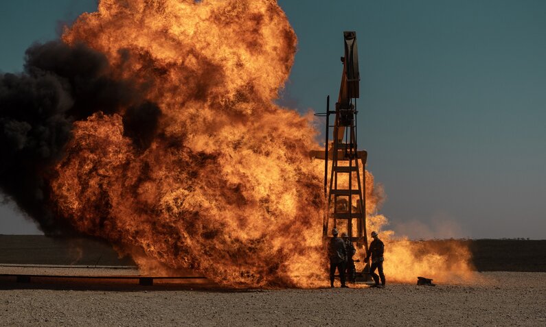 Feuer an einem Ölbohrturm vor blauem Himmel in einer Szene aus der Paramount+-Serie "Landman" | © Paramount+