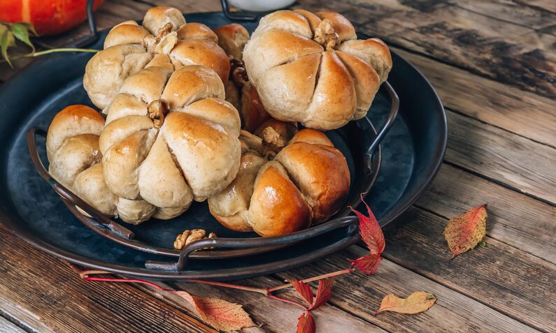 Mehrere kleine Brötchen in Kürbisform auf einem Teller angerichtet in herbstlicher Athmosphäre. | © Getty Images / 	Irina Kozmova