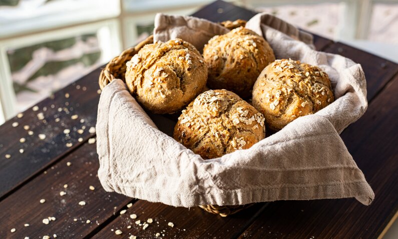 Mehrere Brötchen mit Körnern gestreut in einem Brotkorb auf einem Holztisch. | © Getty Images / Sandra Backwinkel