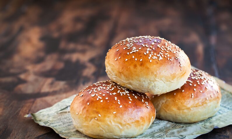 Drei aufeinander gestapelte Burger-Brötchen auf Holzuntergrund. | © Adobe Stock / kate_smirnova