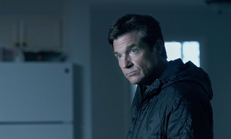 Jason Bateman steht als Marty Byrde in einer Szene aus der Netflix-Serie "Ozark" mit düsterem Blick in einem dunklen Raum. | © Netflix/Steve Dietl