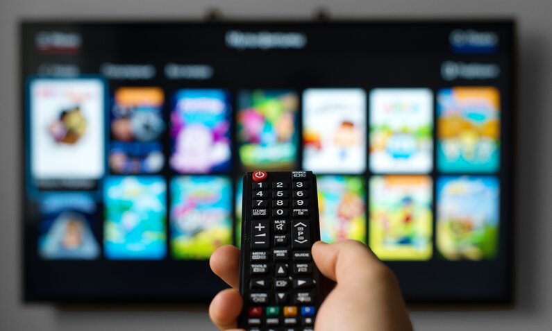 Smart TV im Hintergrund, Fernbedienung im Vordergrund, die auf den Fernseher zeigt | © Getty Images / M-Production