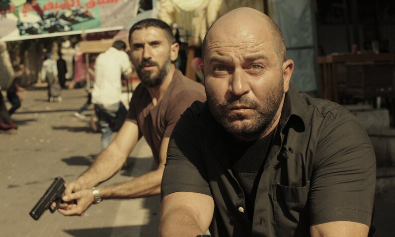 Doron Ben-David und Lior Raz in einer Szene der israelischen Serie "Fauda" in der es um eine militärische Spezialeinheit geht. Die beiden Hauptdarsteller stehen mit gezückten Waffen auf eine belebten, sonnigen Straße | © Netflix