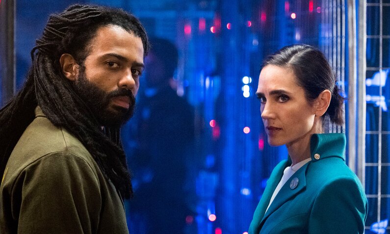 Daveed Diggs und Jennifer Connelly in der TNT Serie "Snowpiercer". Die beiden stehen nebeneinander im einem Rau mit blauem Licht und blinkenden geräten und blicken beide zur Kamera. | © ddp images