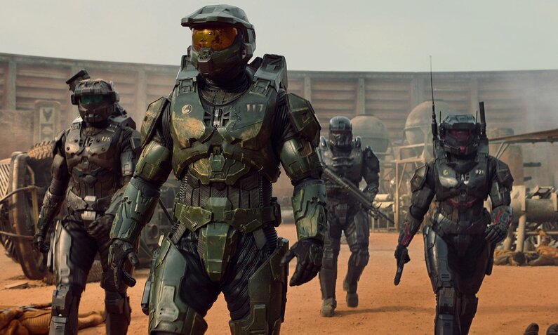 Szene aus der Paramount+ Serie "Halo". Meherer Gestalten in futuristischen militärischen Rüstung mit Helm und Waffen laufen über roten Sand auf uns zu. | © 2022 Microsoft Corporation. All Rights Reserved.