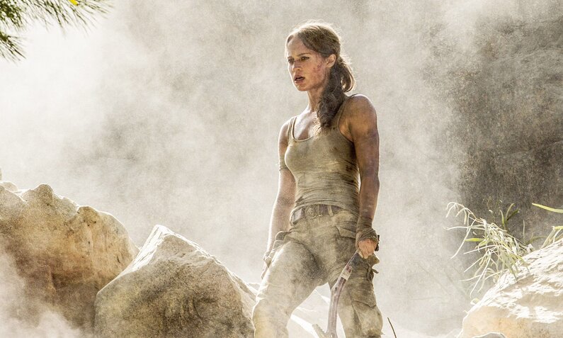 Alicia Vikander als Abenteuer-Archeologin Lara Croft im Film "Tomb Raider" von 2028. Die heldin steht in einer grauen Staubwolke, trägt Cargopants und eine Tanktop, Kleider, Gesicht und Arme sind schmutzbedeckt. | © ddp images/LMKMEDIA
