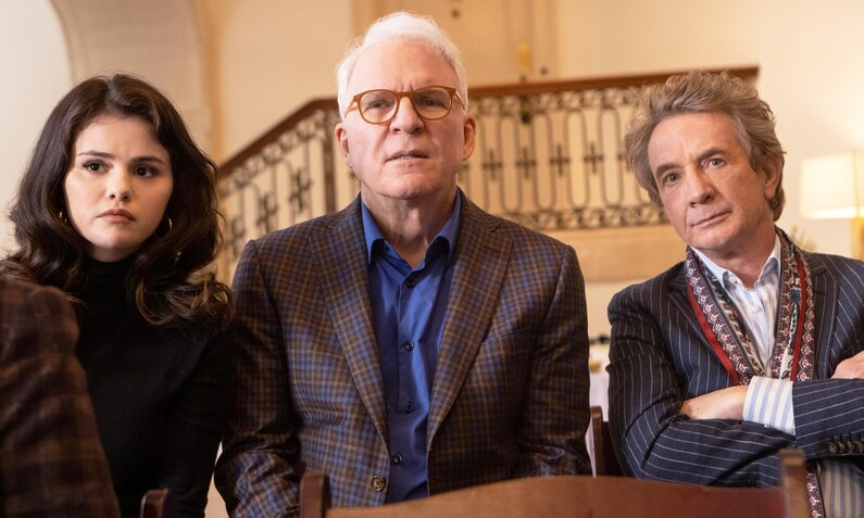 Steve Martin. Selena Gomez und Martin Short in der dritten Staffel der Serie "Only Murders in the Building". Sie stehen nebeneinander im Inneren eines Hauses, im Hintergrund ist ein prächtiger Treppenaufgang zu sehen. | © Disney+