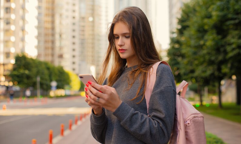 Eine junge Frau nutzt ein iPhone auf der Straße. | © Getty Images/Mensent Photography