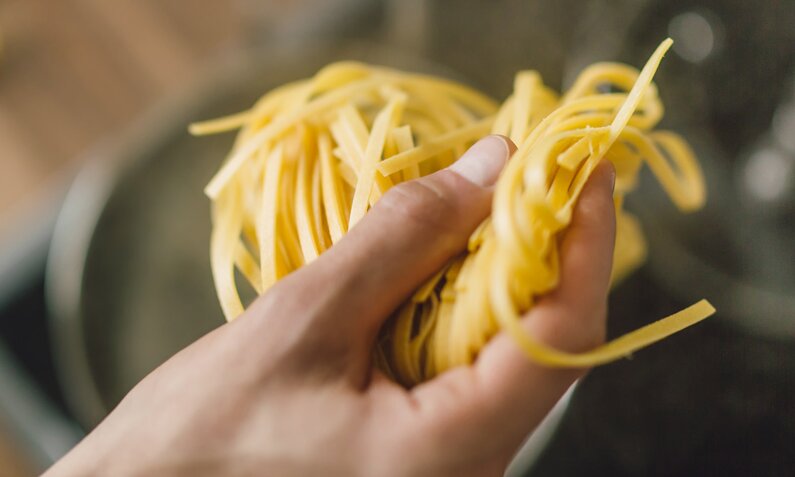 Eine Hand hält Pasta über einen Topf mit kochendem Wasser | © Getty Images/nerudol