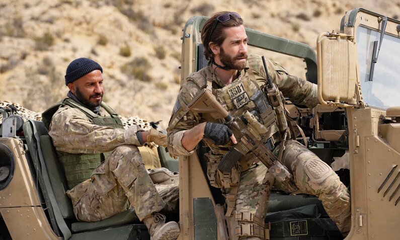 Dar Salim und Jake Gyllenhaal mit Waffen und in Militär-Camouflage-Kleidung in einem Jeep in einer Filmszene aus "Guy Ritchies Der Pakt" | ©  ddp images/LMKMEDIA Ltd.