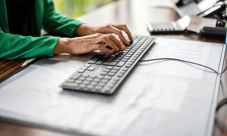 Eine Frau in grüner Bluse schreibt auf einer Tastatur, die per Kabel mit einem Computer verbunden ist. | © Getty Images/Luis Alvarez