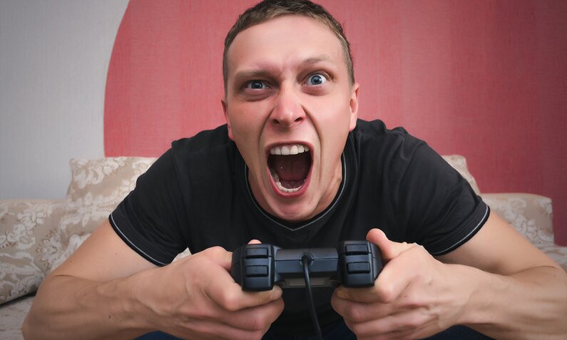 Junger Mann hält einen Game-Controller und brüllt wütend herum. | © Getty Images