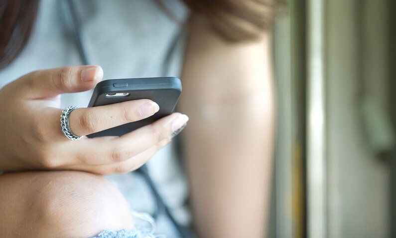 Frau hält ein Smartphone in der Hand, zu erkennen ein Knie durch zerrissene Jeans. | © Getty Images/pooraya