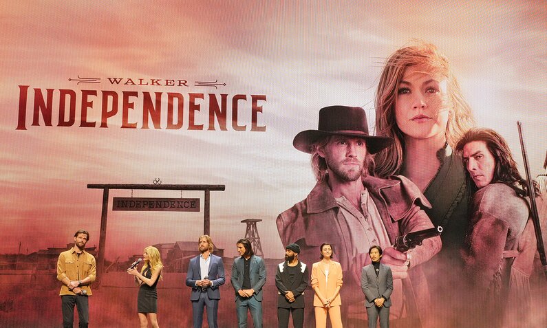 Produtzent Jared Padalecki und die Darsteller*innen Katherine McNamara, Matt Barr, Justin Johnson Cortez, Philemon Chambers, Katie Findlay und Lawrence Kao stehen beim Presseevent zu "Walker: Independence" vor einem gigantischen Plakat zur Serie auf einer großen Bühne  | © Getty Images/Kevin Mazur