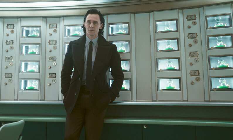 Tom Hiddleston lehnt in der Marvel/Disney+ Serie "Loki" an einer Wand mit lauter kleinen Fenstern | © Marvel/Disney+
