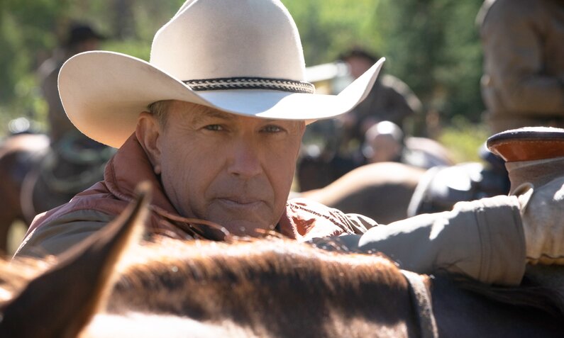 Nahaufnahme von Kevin Costner mit Cowboyhut über einen Pferderücken blickend in einer Szene der Paramount Serie "Yellowstone" | © Paramount Network