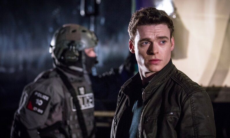 Richard Madden als Personenschützer in einer Szene der BBC Serie "Bodyguard". Madden steht bei Nacht in dunkler Kleidung im Vordergrund ein Mitglied einer Spezialeinheit in voller Einsatzmontur | © Netflix/Sophie Mutevelian/World Productions