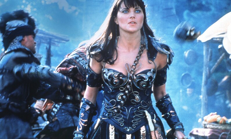 Lucy Lawless in Rüstungsdress vor blauem Hintergrund in einer Szene aus der Serie "Xena – Die Kriegerprinzessin" | © ddp images