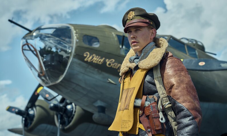 Austin Butler steht in Fliegermontur vor einem kleinen Militärflugzeug aus dem zweiten Weltkrieg in einer Szene aus der Apple TV+ Serie "Masters of the Air" | © Apple TV+