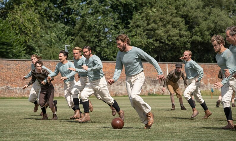 Eine Männer-Mannschaft in hellblauen Trikots rennt mit Ball über eine Wiese in einer Szene der Netflix Serie "The English Game" | © Netflix/Oliver Upton