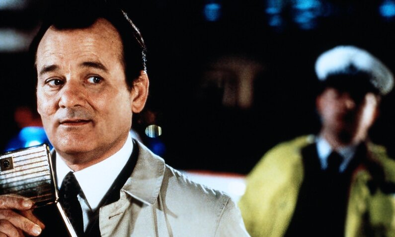 Im Vordergrund der Szene aus dem Kinofilm "Agent Null Null Nix" ist Bill Murray zu sehen, der bei Nacht draußen steht und leicht lächelt. Im Hintegrund ist ein Polizist mit einer Warnweste zu sehen. | © ddp images