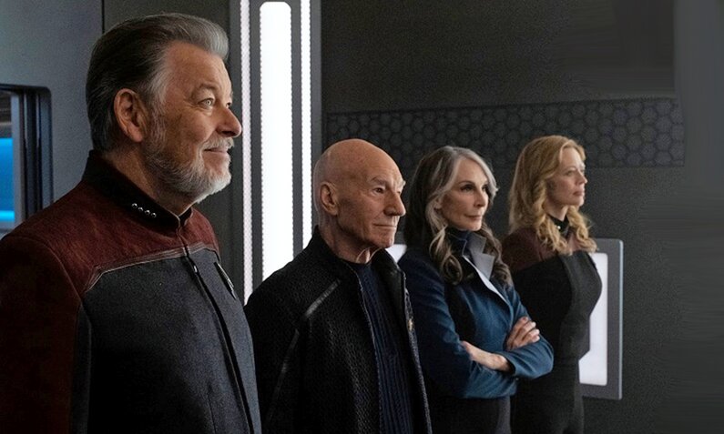 Jonathan Frakes, Patrick Stewart. Gates McFadden und Jeri Ryan stehen nebeneinander in einem dunklen Raum an Bord eines Raumschiffs in einer Szene aus der Serie  "Star Trek: Picard" | © Paramount