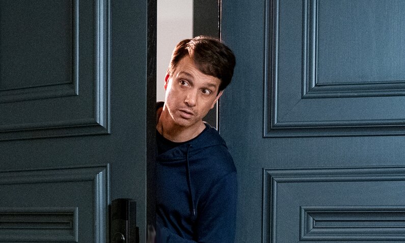 Ralph Macchio lugt durch eine nur wenig geöffnete Tür in einer Szene aus der Netflix-Serie "Cobra Kai" | © Netflix/Curtis Bonds Baker
