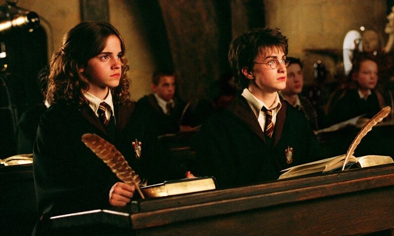 Emma Watson und Daniel Radcliffe sitzen in einer Szene aus dem Kinofilm "Harry Potter und der Gefangene von Askaban" in Schuluniformen im Klassenzimmer nebeninander  | © ddp images