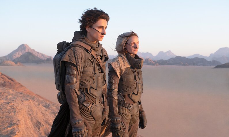 Timothy Chalamet und Rebecca Ferguson in futuristischer Kleidung vor einer Wüstenlandschaft in einer Szene des Kinofilms "Dune" | © ddp images/Capital Pictures