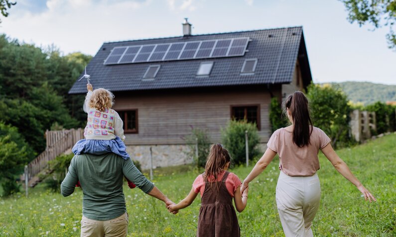 Familie steht vor einem Haus mit einer Photovoltaikanlage auf dem Dach | © Getty Images/Halfpoint Images