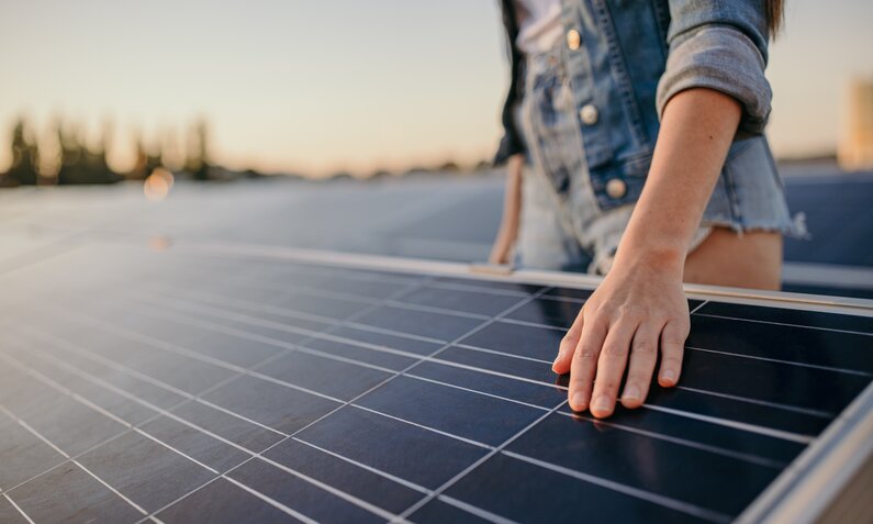 Frau berührt mit ihrer Hand das Solarmodul einer Solaranlage | © Getty Images/SimonSkafar