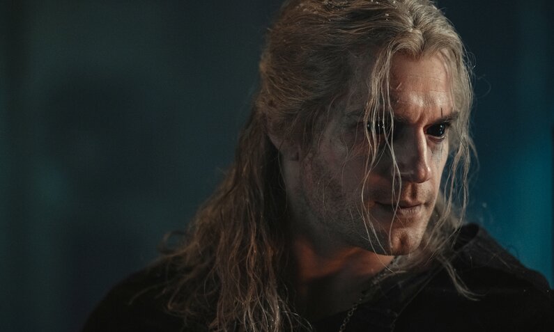Nahaufnahme von Henry Cavill mit langem weißen Haar und ernstem Gesicht vor schwarzem Hintergrund in einer Szene der Netflix-Serie "The Witcher" | © Netflix/Jay Maiment