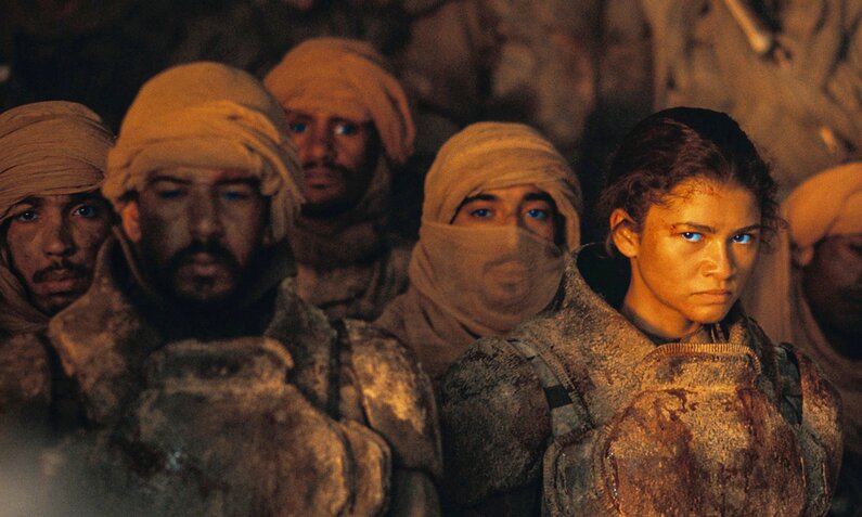 Imago steht mit grimmigem Gesicht  in einer Menge von Wüstenbewohnern in einer Szene des Kinofilms "Dune Part 2" | © Imago Images/Landmark Media