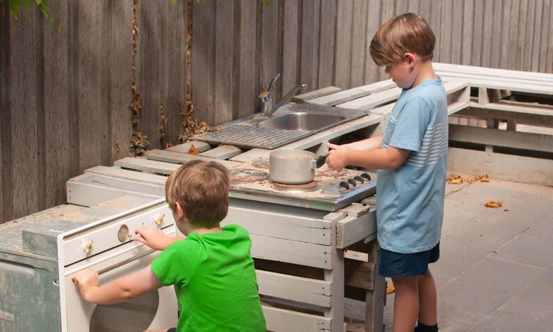 Kinderküche im Freien: Zwei Jungen experimentieren mit Kochgeschirr auf altem Herd. | © iStock / Getty Images Plus / CarrieCaptured