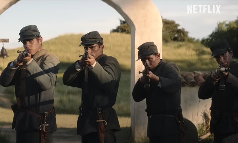 Soldaten stehen in einer Reihe mit Gewehr im Anschlag in einer Szene aus dem Trailer zur Netflix Serie "One Hundred Years of Solitude" | © Netflix auf YouTube/Screenshot Trailer