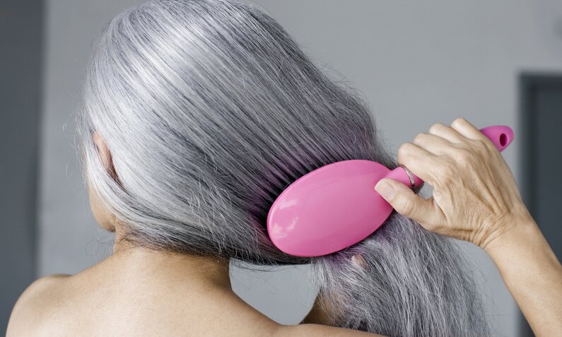 Frau mit glänzendem grauen Haar bürstet sich die Haare | © Getty Images/ Patrik Giardino