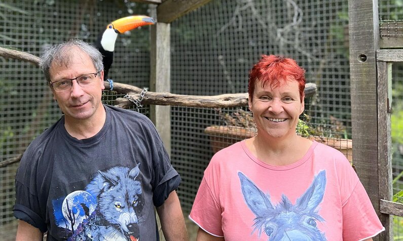 Zwei Personen mit bunten T-Shirts und fröhlichem Gesichtsausdruck stehen vor einem Vogelkäfig. | © RTL