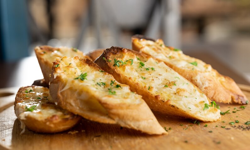 Knoblauchbaguette ohne Hefe in Stücke geschnitten auf einem Holzbrett. | © Getty Images / Justin Ong