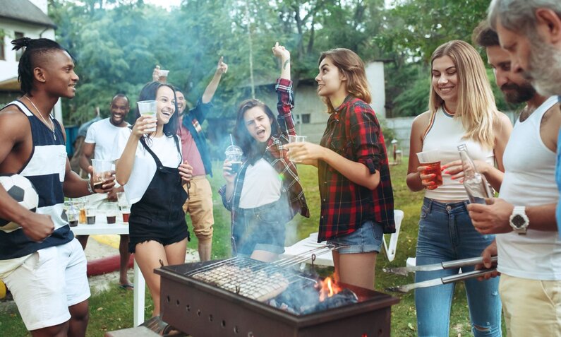 Lachende Freunde beim Grillen im Garten, mit Getränken und entspannter Stimmung. | © master1305/stock.adobe.com