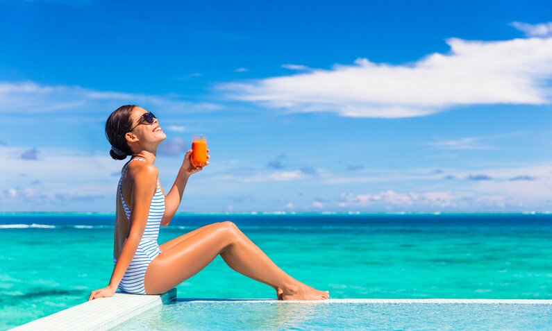 Entspannte Urlauberin mit Drink am türkisblauen Meer unter strahlend blauem Himmel. | © Getty Images/ Maridav