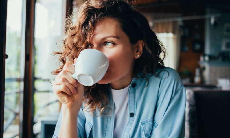 Frau mit lockigen Haaren trinkt Kaffee aus einer Tasse. | © Getty Images / 	iprogressman