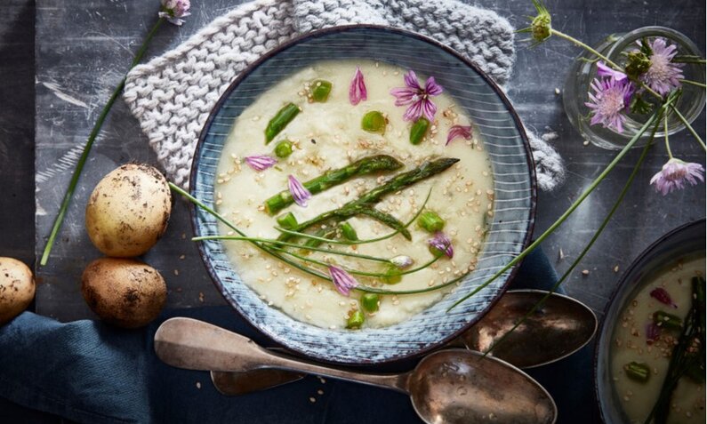 Spargelcremesuppe in einem Suppenteller, darin Spargelstücke und Blütenblätter. | © Getty Images / REDA&CO / Kontributor