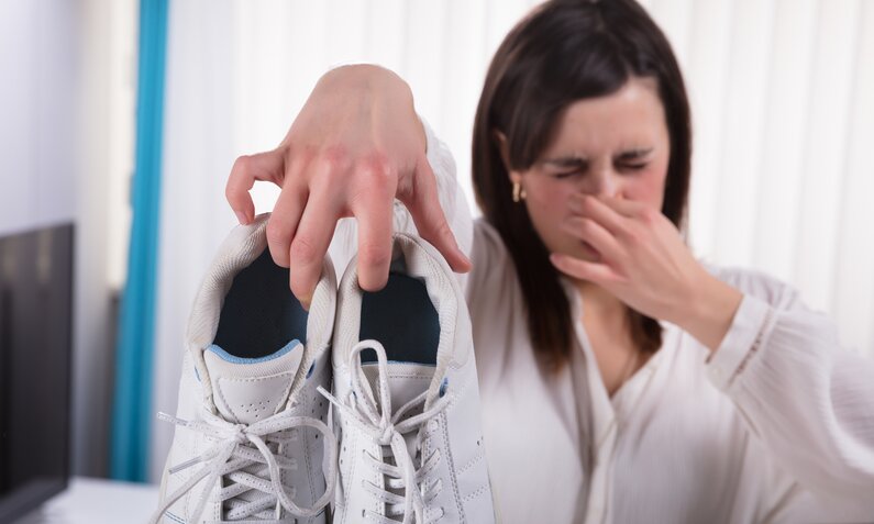 Frau zeigt Schuhe und hält sich dabei die Nase zu | © Getty Images/ AndreyPopov