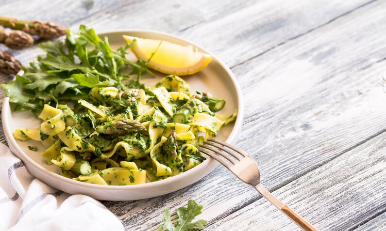 Auf einem weißen Teller sind frische Tagliatelle mit grünem Spargel und Spinat angerichtet. | © Getty Images / Ivannag82