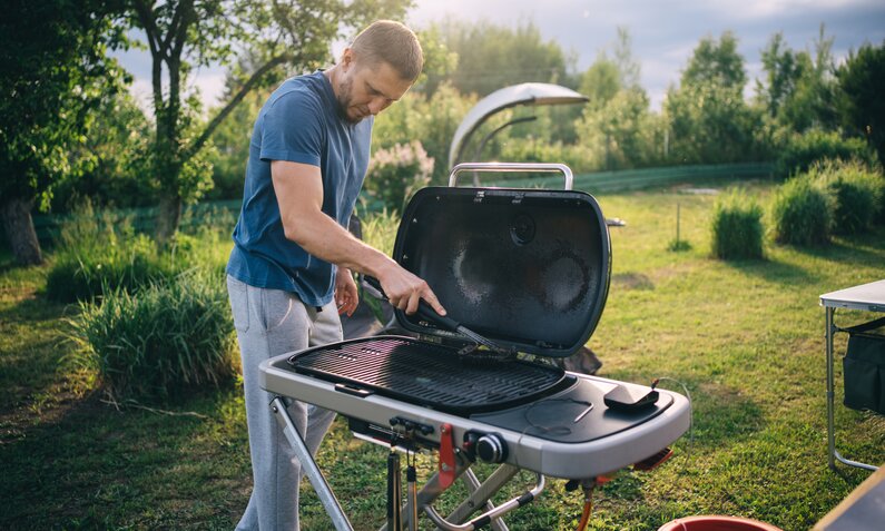 Mann reinigt Grill im Garten | © Getty Images/ Svetlana Repnitskaya