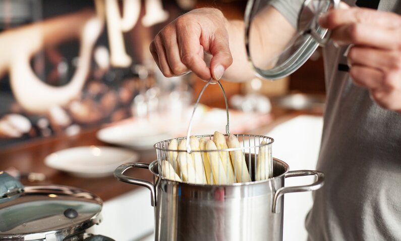 Hände halten weißen Spargel in Spargeltopf hinein zum Kochen. | © Getty Images / Kathrin Ziegler