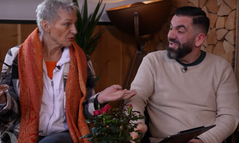 Ältere Dame mit kurzem grauen Haar und orangefarbenem Schal diskutiert gestikulierend mit einem bärtigen Mann in einem hellen Pullover. | © Screenshot Vox/RTL+ 