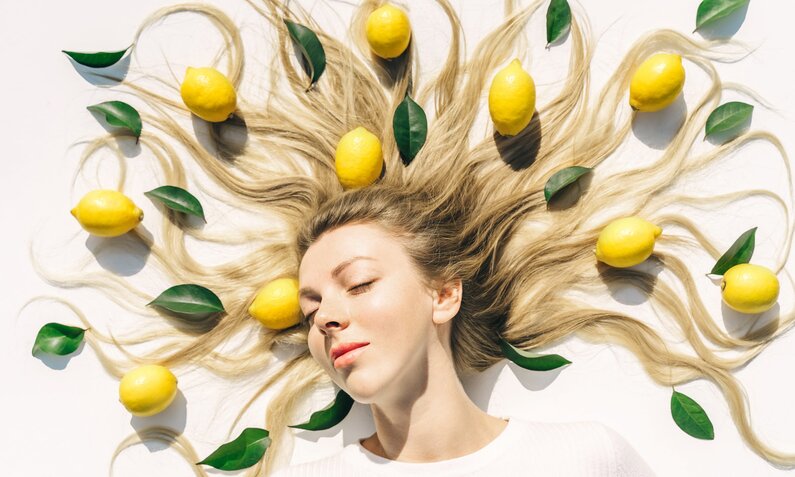 Porträt einer jungen Frau, die ruhig liegt, mit Zitronen und Blättern kunstvoll in ihrem blonden Haar arrangiert | © Getty Images/ Tatiana Maksimova